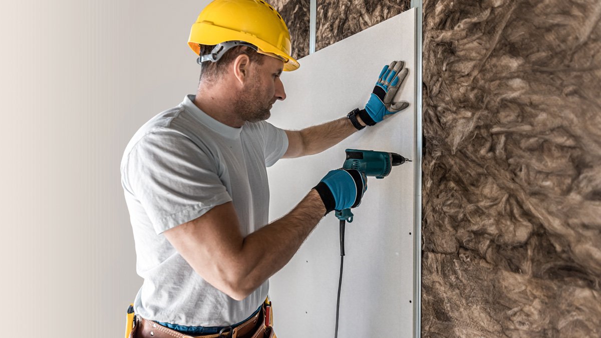 A professional wearing a yellow hardhat installing white drywall in an El Paso home.