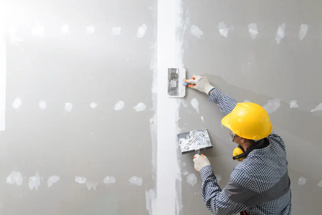 A person in a yellow hard hat installing drywall in an El Paso home.