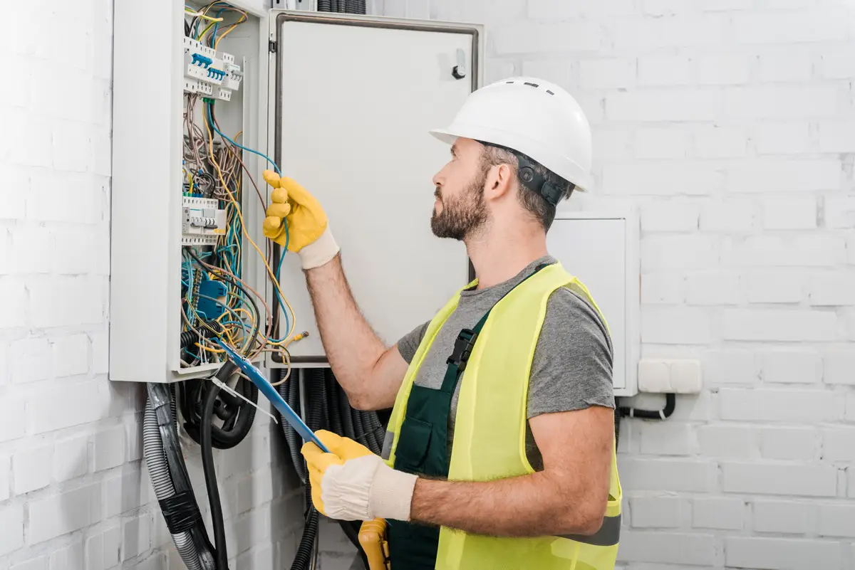 A person in a white hard hat and yellow vest performing electrical services at a home in El Paso.