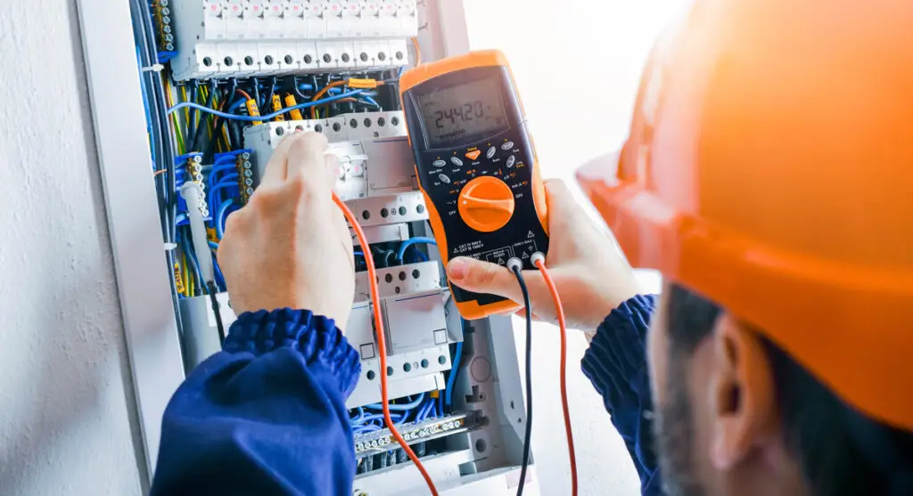 A person in an orange hardhat performing electrical services at an El Paso home.