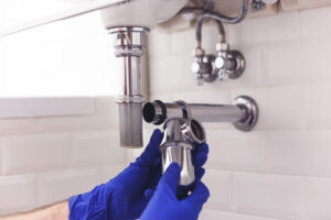 A person’s hands in blue gloves making a plumbing repair to a sink in an El Paso home.