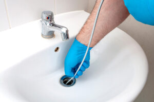 A plumber wearing blue gloves unclogging a sink in El Paso.