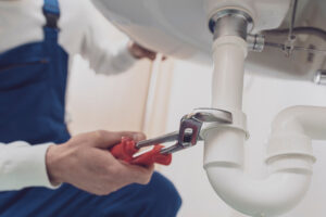 A plumber using a wrench on a white pipe under the sink in El Paso.