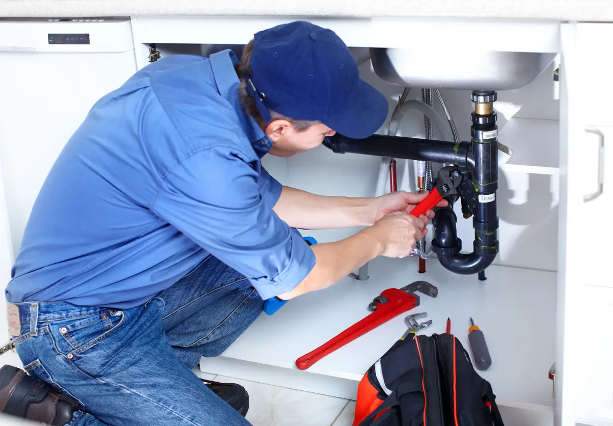 A plumber in a blue shirt using a wrench on sink pipes in El Paso.