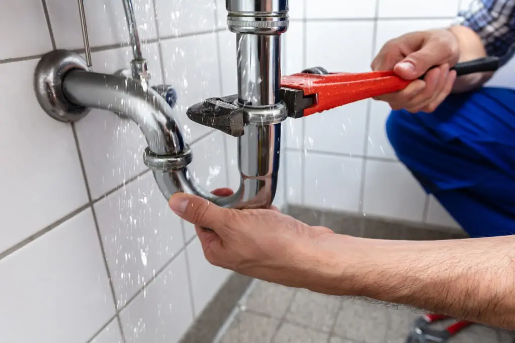 A plumber's hands are using a red wrench to fix a leaking pipe in an El Paso home.