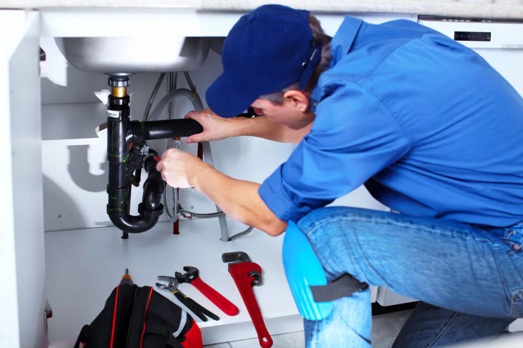 A plumber in a blue shirt performing plumbing repair under a sink in El Paso.